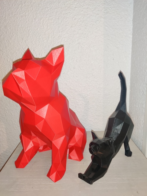 Figurine d'un chat noir posé sur un meuble avec à ses cotés un grand bulldog rouge.