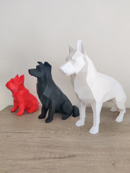 Figurines de chiens, pour la SPA de la Mayenne, en ligne posées sur un meuble. A gauche, une petite rouge, au centre un plus grande en noire et à droite une plus grande encore qui est blanche. 