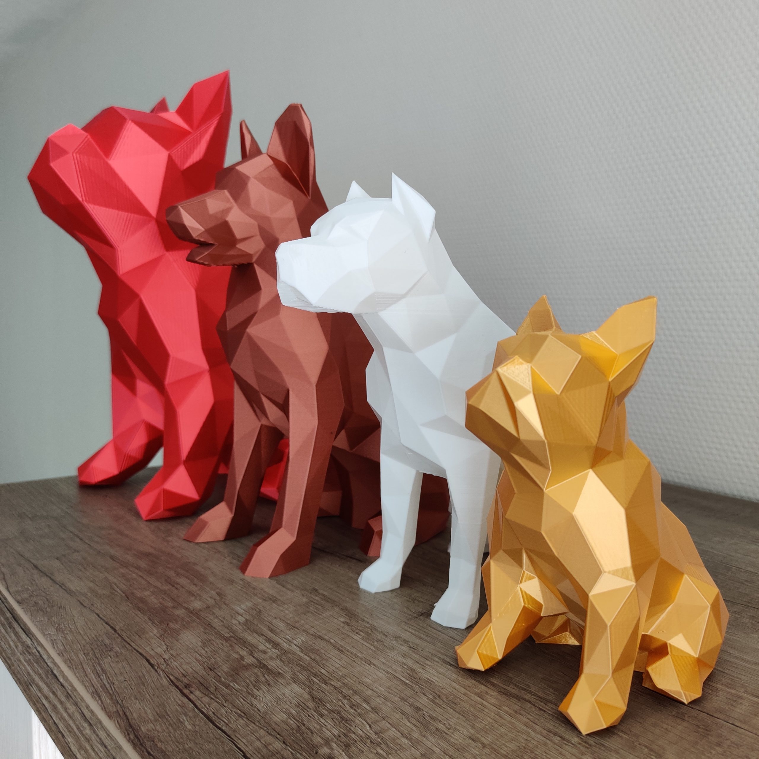 Figurines de chiens, pour la SPA de la Mayenne, en ligne posées sur un meuble. La plus grande est rouge, ensuite une cuivre puis une blanche et pour finir une en couleur or.